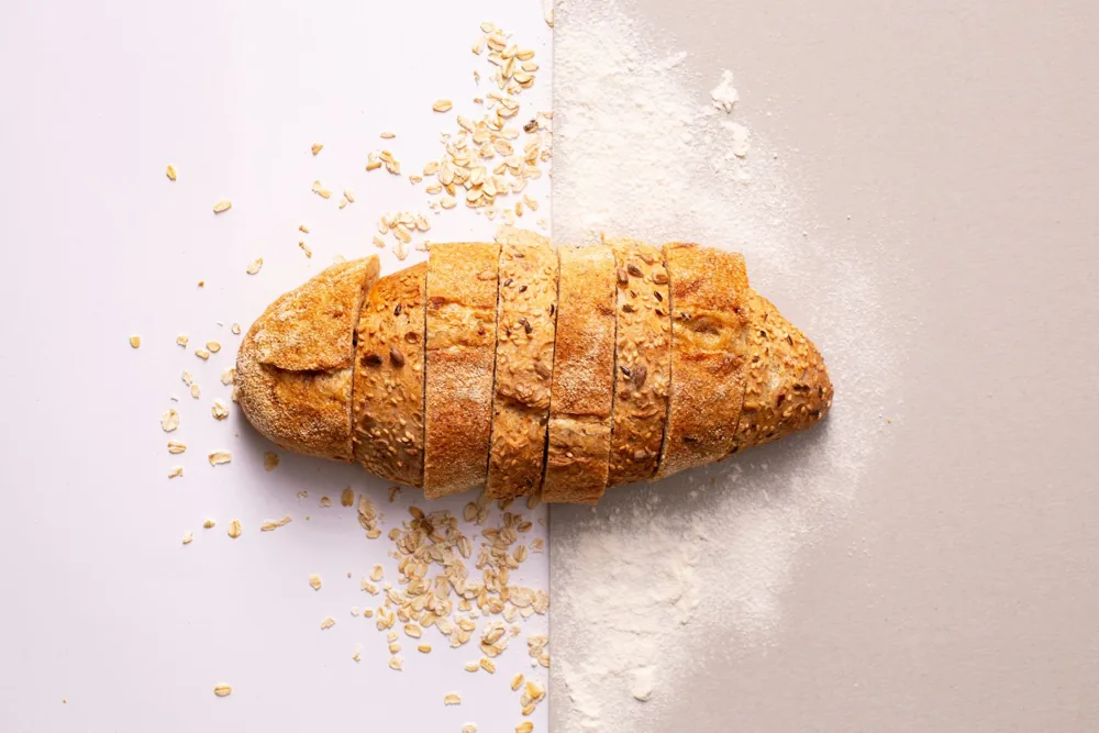 A golden sliced loaf scattered with crumbs on a pale tabletop