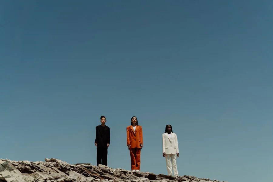 Three people in ink, orange and pale suits against an open blue sky